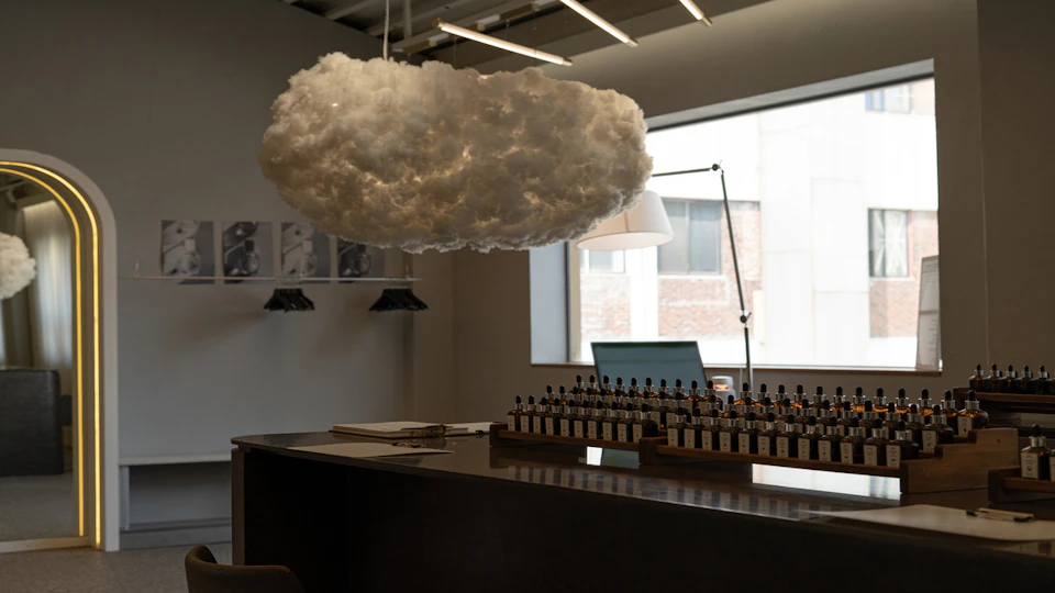 A modern interior with a cloud-shaped light fixture above a counter holding rows of small bottles and a laptop in a lit space.