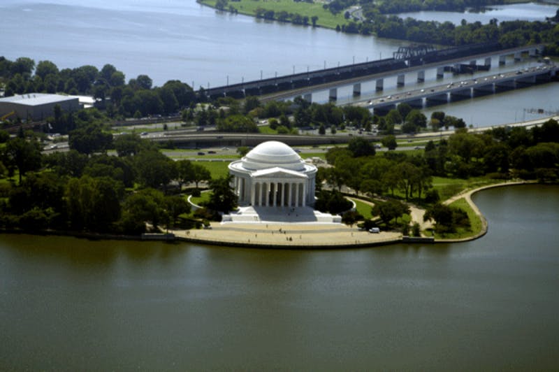 Flygfoto över Thomas Jefferson Memorial omgiven av vatten och grönska med en bro och en motorväg i bakgrunden.