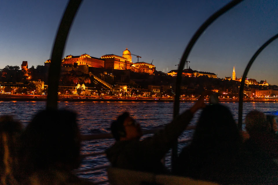 People on a boat at night with a view of a lit-up historic building on a hill across the water.