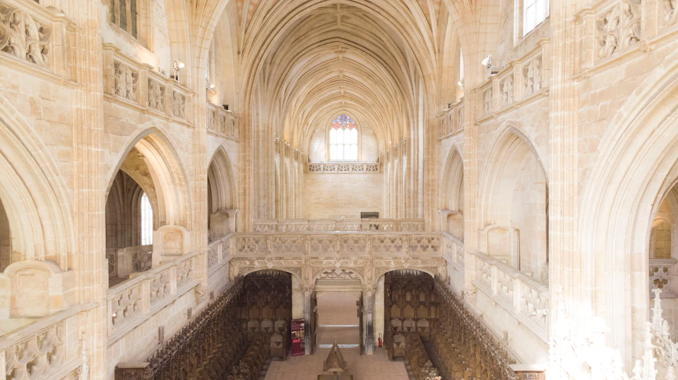 A spacious Gothic cathedral interior with high arched ceilings, intricate stonework, and wooden choir stalls.