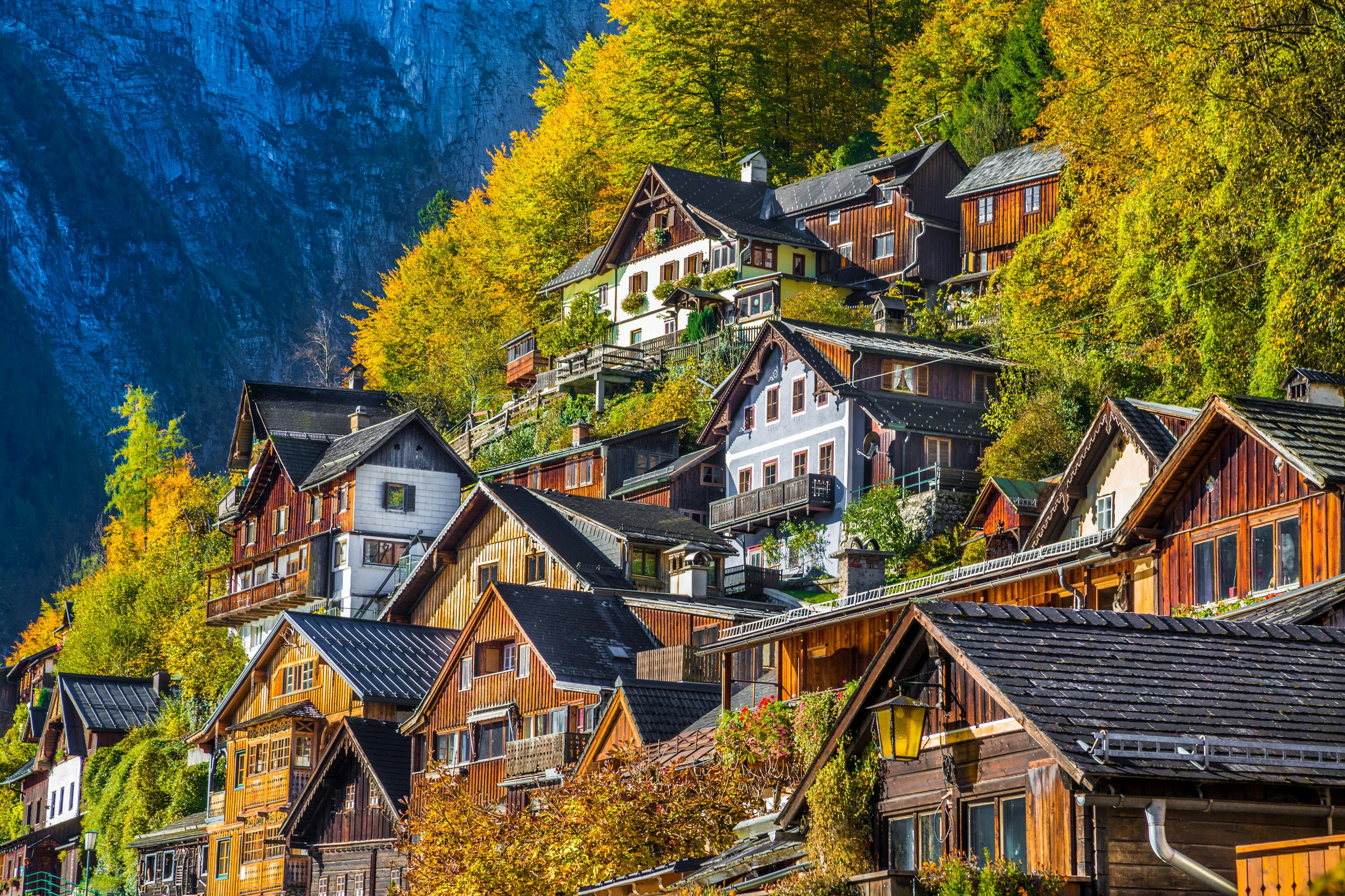 Un village pittoresque à flanc de colline avec des maisons en bois et colorées entourées d'arbres d'automne et d'un arrière-plan montagneux.