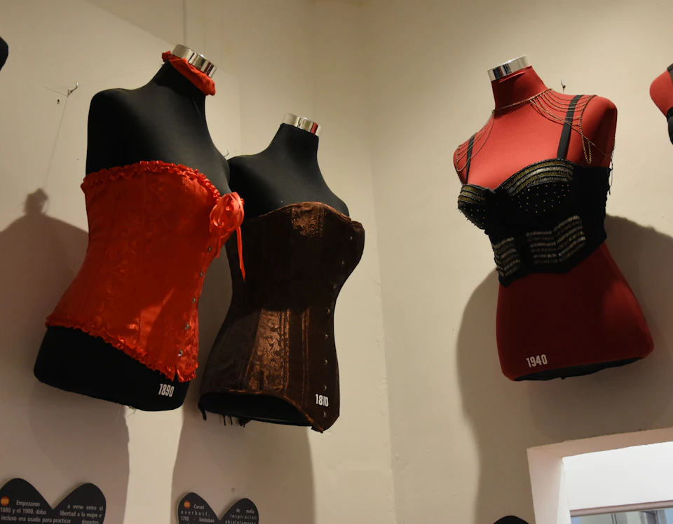 Three mannequins display vintage corsets: a red one from 1980, a brown one from 1890, and a black and red one from 1940.