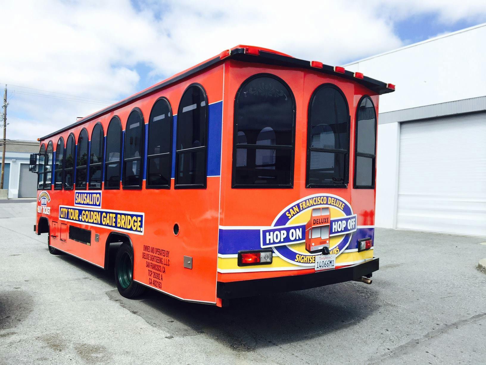 Un bus touristique "Hop-on Hop-off" orange vif garé sur un terrain, avec des fenêtres arquées et des panneaux indiquant la visite du Golden Gate Bridge.
