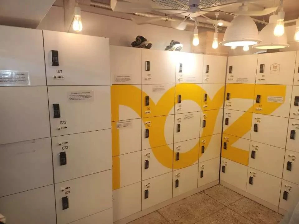 A set of white lockers with black keypad locks, featuring a large yellow design, under hanging light fixtures.