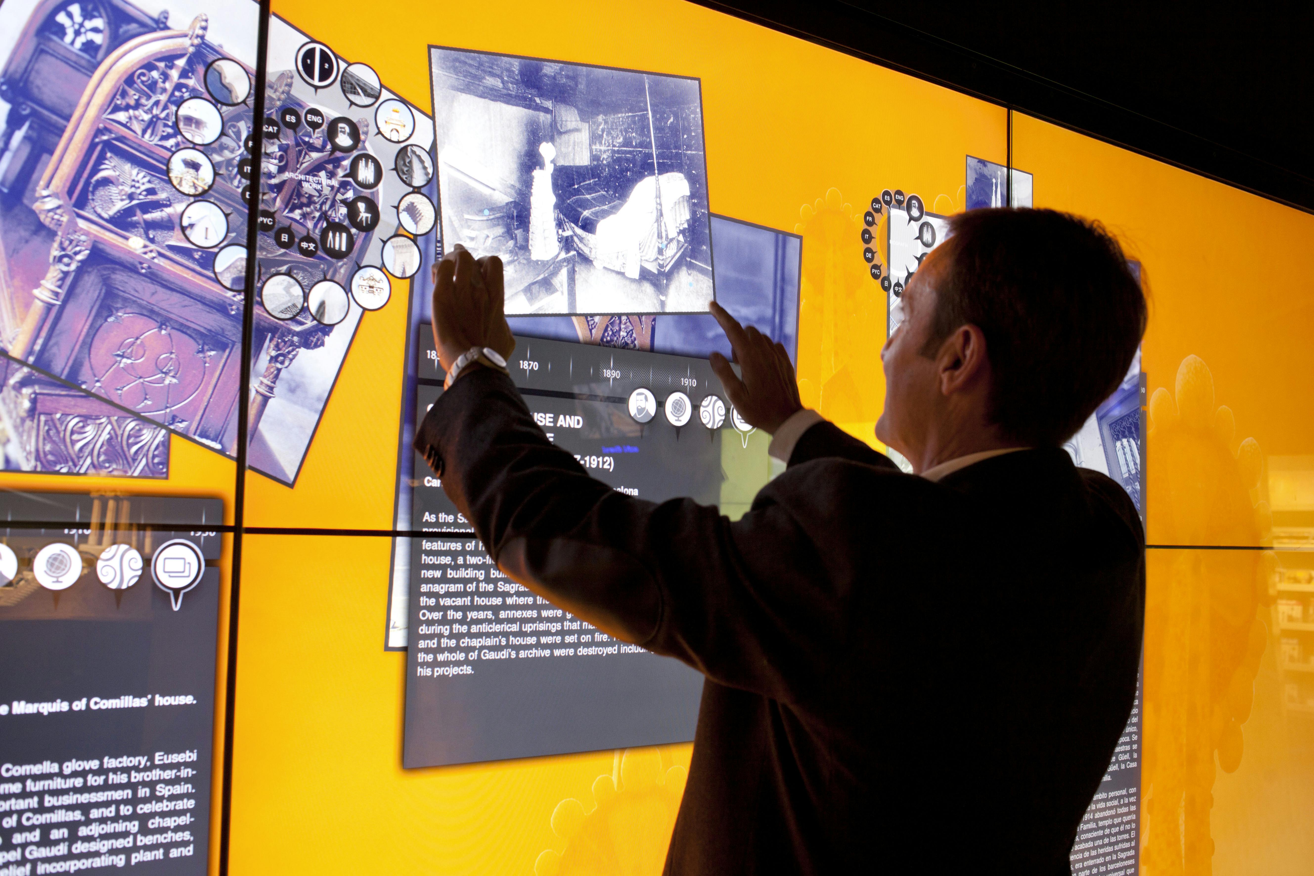 한 사람이 주황색 배경에 흑백 이미지와 다양한 아이콘을 표시하는 대형 터치 스크린과 상호 작용합니다.