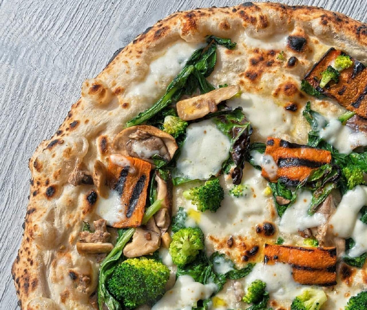 Пицца с овощами на гриле, включая брокколи, шпинат, грибы и плавленый сыр на деревянной поверхности.