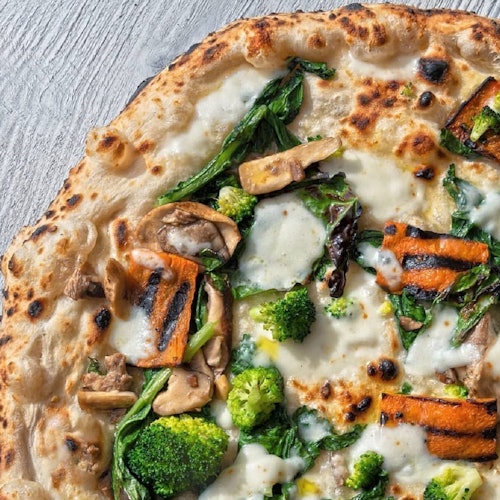 Pizza topped with grilled vegetables, including broccoli, spinach, mushrooms, and melted cheese on a wooden surface.