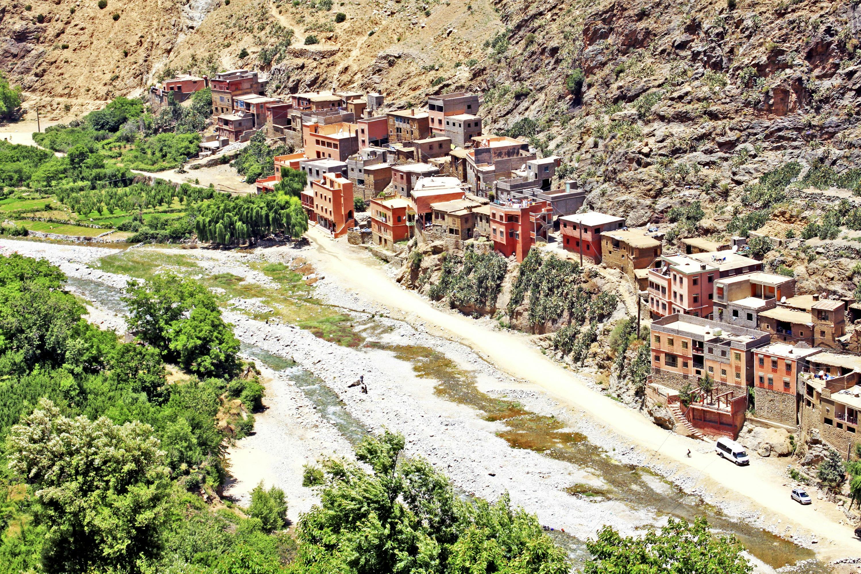 Cluster of colorful houses built on a mountainside, with a narrow river and green trees in the foreground.