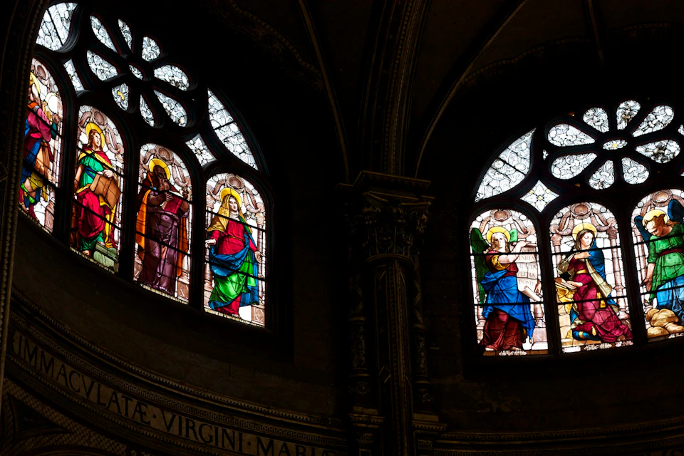 Stained-glass windows in an ornate, arched church interior depicting religious figures in vibrant robes.