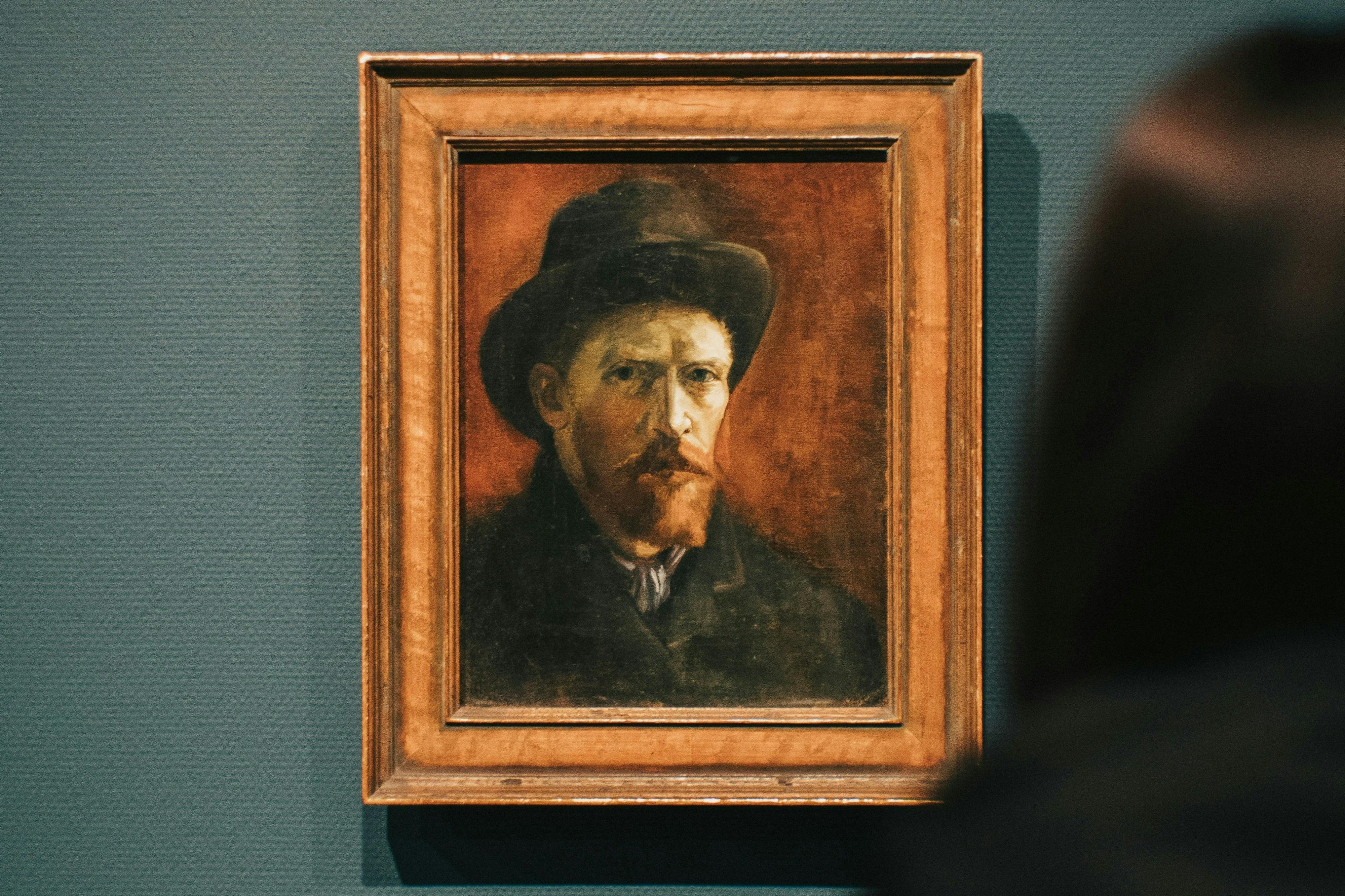 墙上挂着一个戴着帽子、留着胡子的男人的肖像画。 一个人的轮廓部分可见。