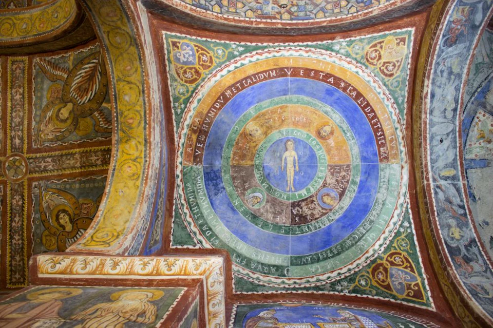 Colorful ceiling with concentric circles featuring a human figure in the center, surrounded by Latin text and ornate designs.