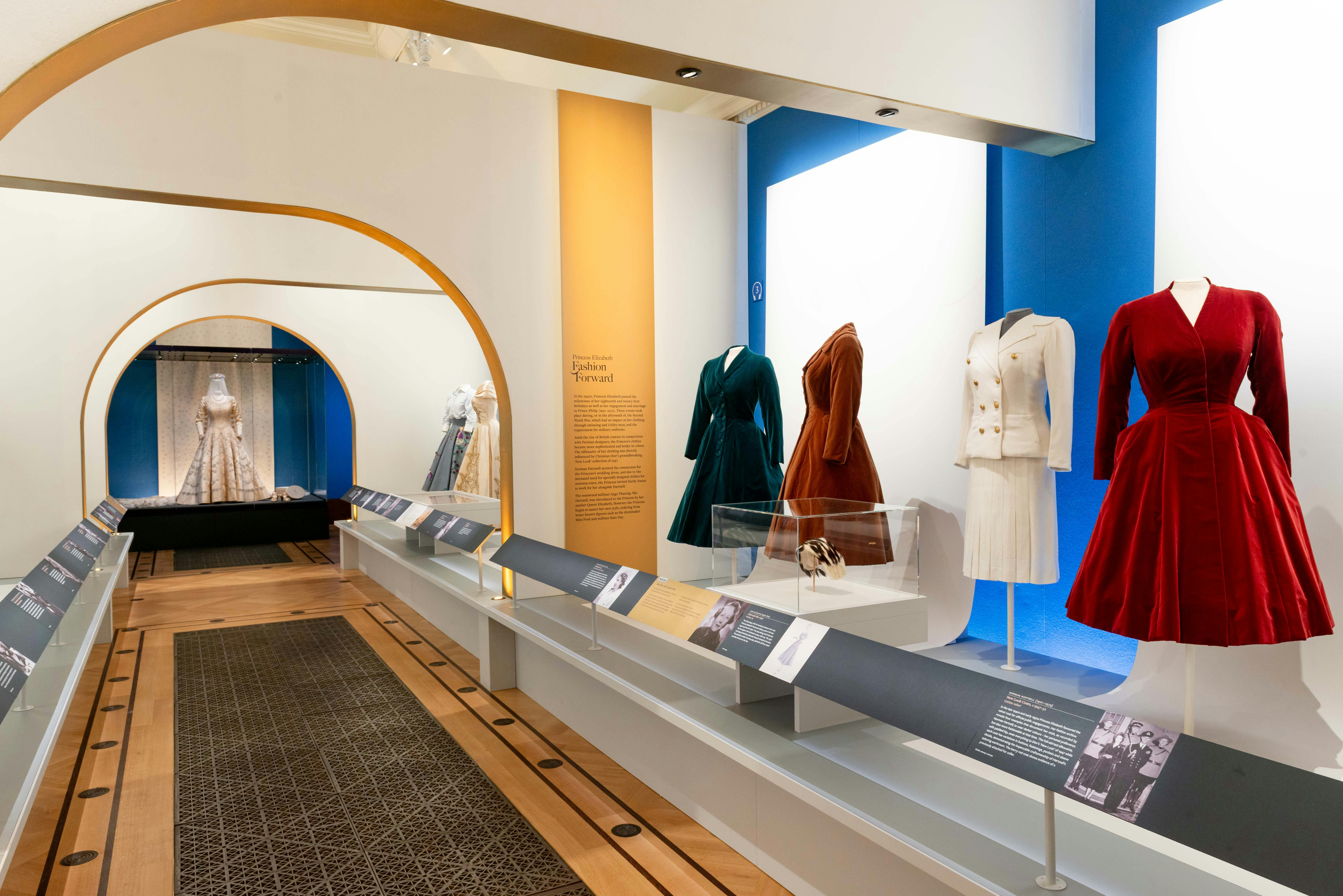 Έκθεση του μουσείου με vintage φορέματα σε μανεκέν, με περιγραφικά πάνελ και διακοσμητική αψίδα στο παρασκήνιο.