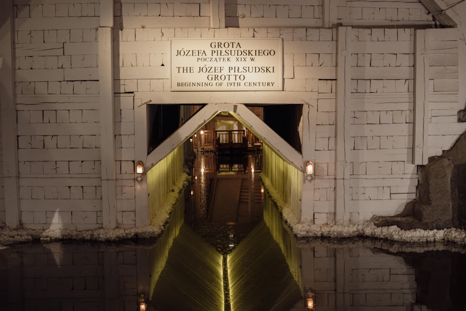 Entrance to the Józef Piłsudski Grotto with illuminated walls and a reflection of the archway in the water below.