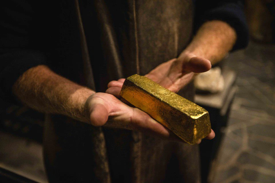 A person holds a large gold bar with both hands in a dimly lit environment.