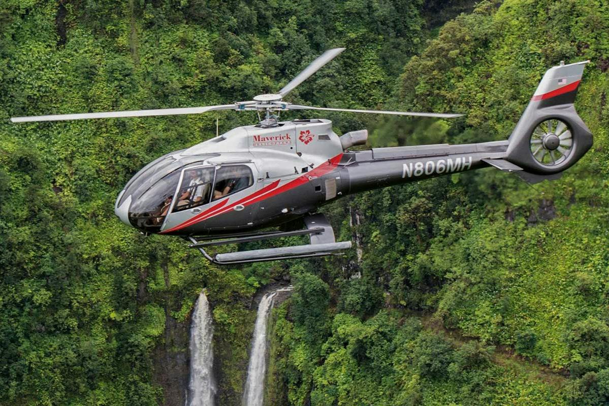 En helikopter som flyger över ett skogsområde med synliga vattenfall i bakgrunden.