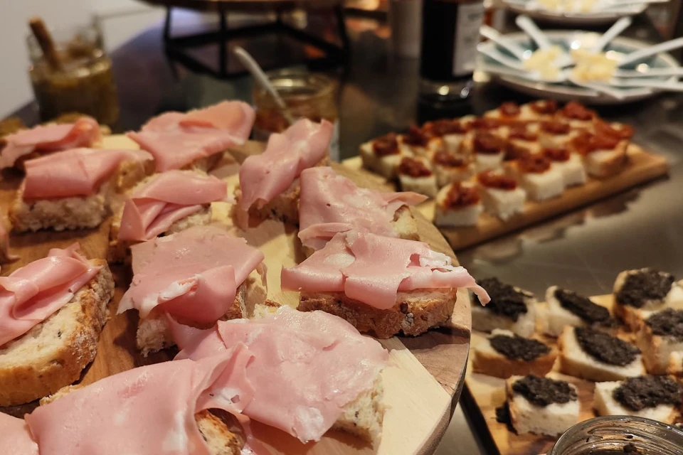 Slices of bread topped with thinly sliced ham and various other toppings on a table ready to be served.