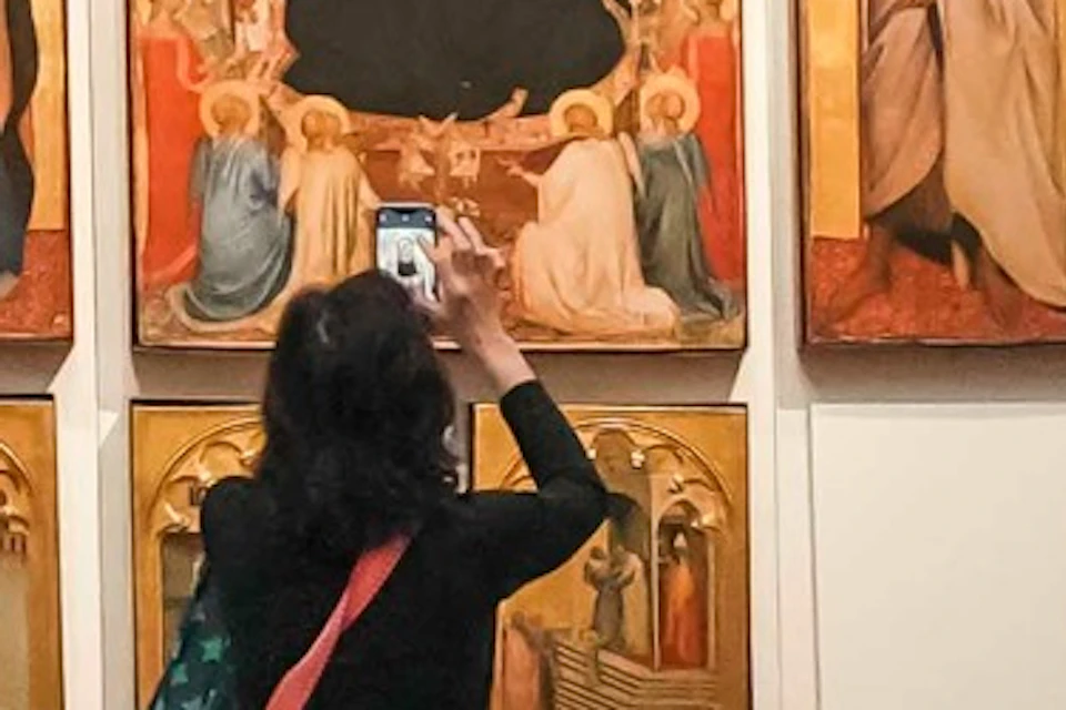 People viewing religious paintings in a museum gallery with walls displaying artwork and a tiled floor.