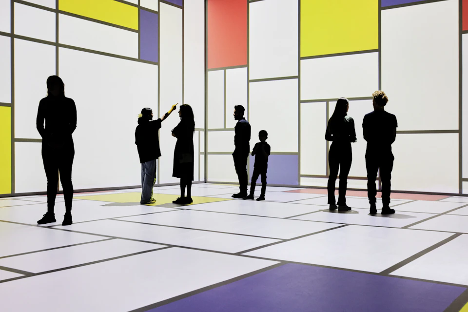 People standing and interacting in a room with large white walls featuring colorful geometric patterns.