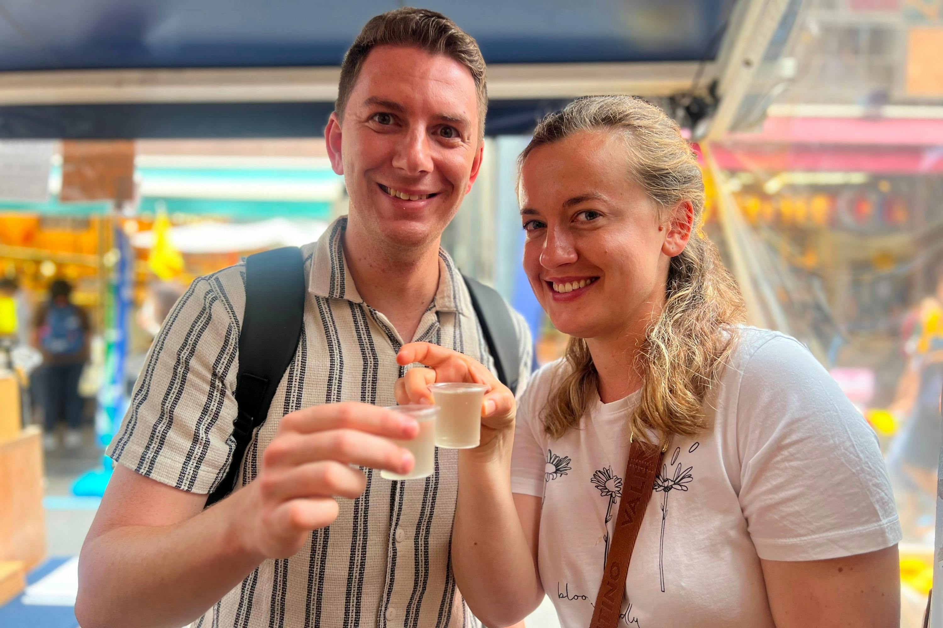 Two people smiling and holding small glasses in a casual outdoor setting.