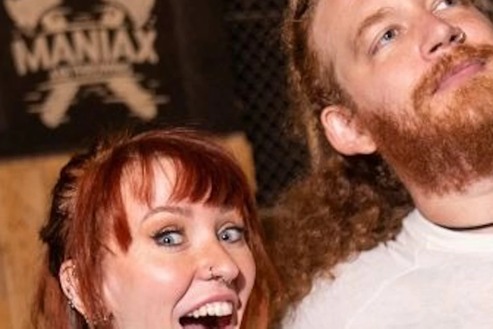 Two people holding axes pose enthusiastically in an axe-throwing venue with wooden targets in the background.
