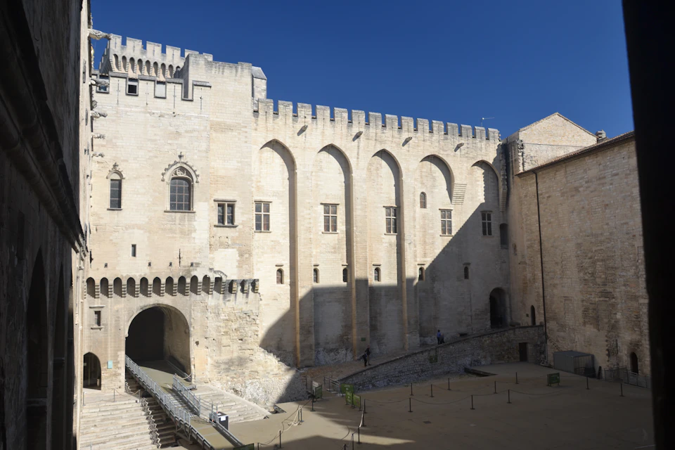 Historic stone courtyard with an archway and rows of arched windows on a castle-like building under a clear blue sky.