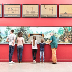 Fem personer, inklusive barn och vuxna, står framför en museiutställning med diorama och informationsskyltar.