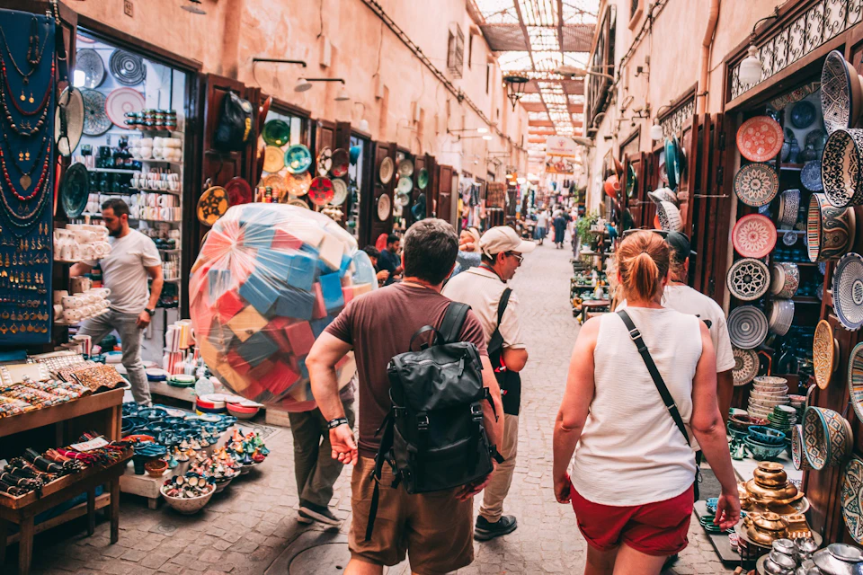 People walking through a busy, covered market street with shops displaying pottery and colorful items on both sides.