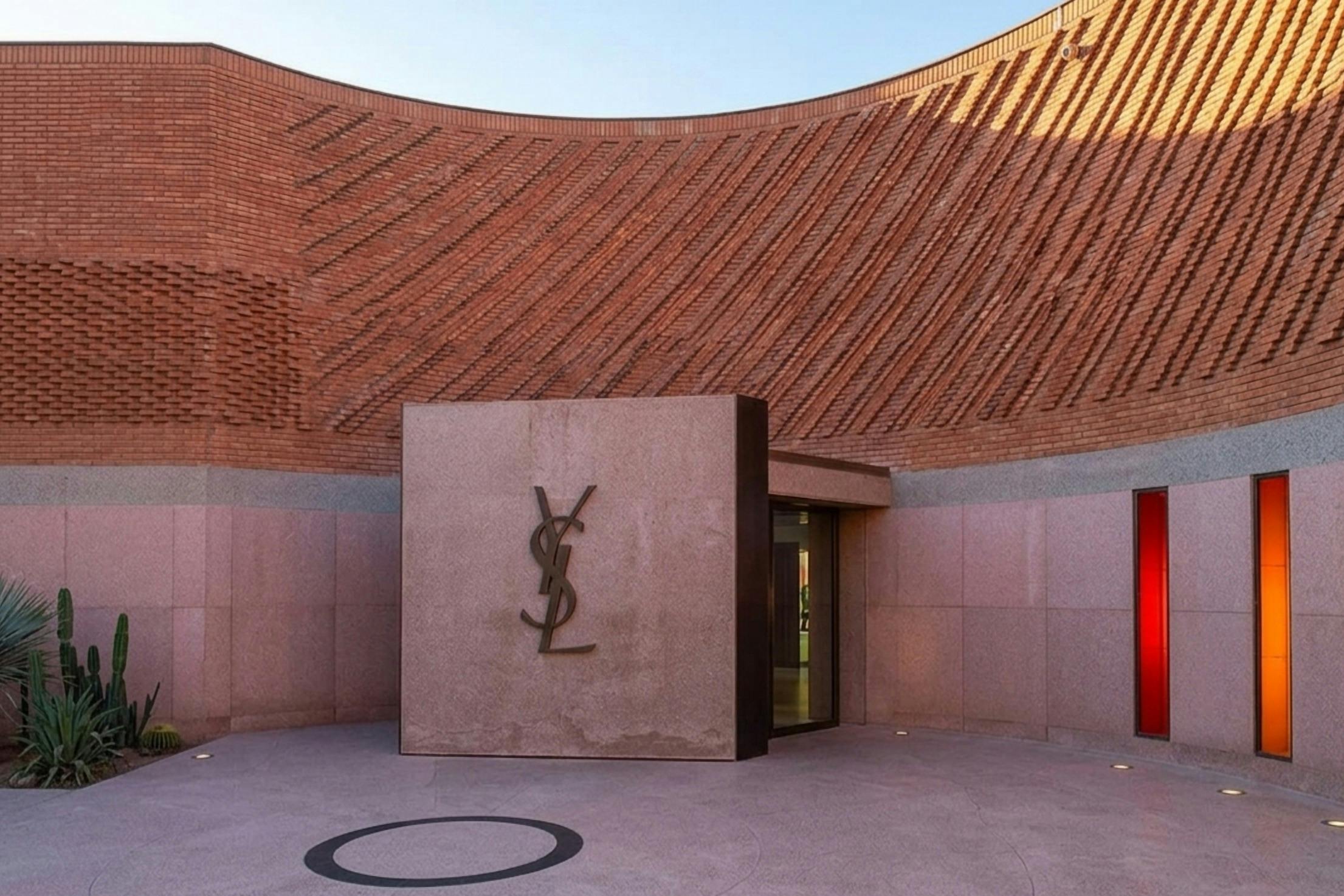 A modern building with a textured brick wall and a monogram logo "YSL" on a stone slab near an entrance.