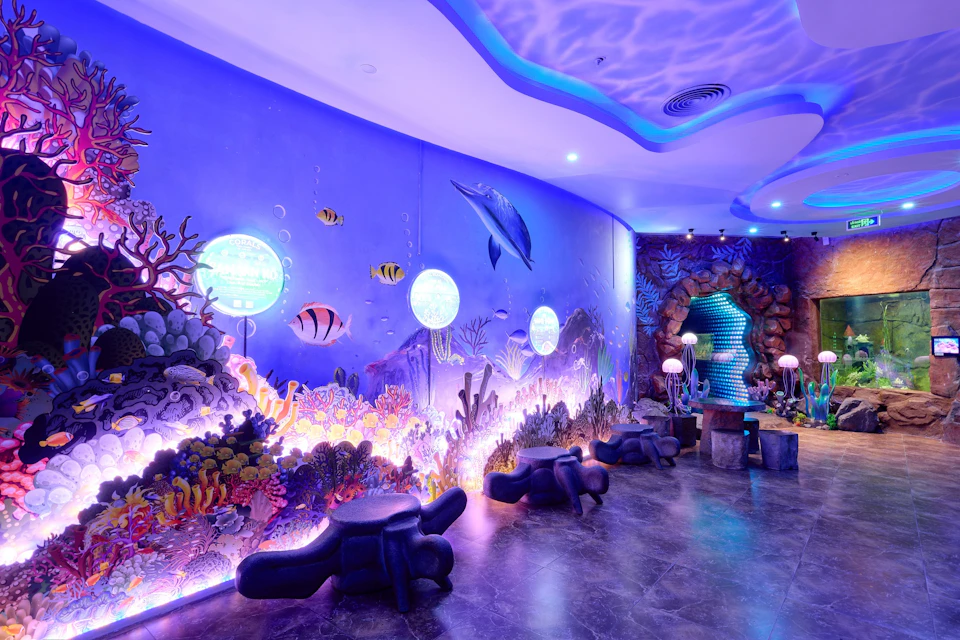 An underwater-themed room with glowing blue lighting, wall art of marine life, and decorative jellyfish-shaped lamps.