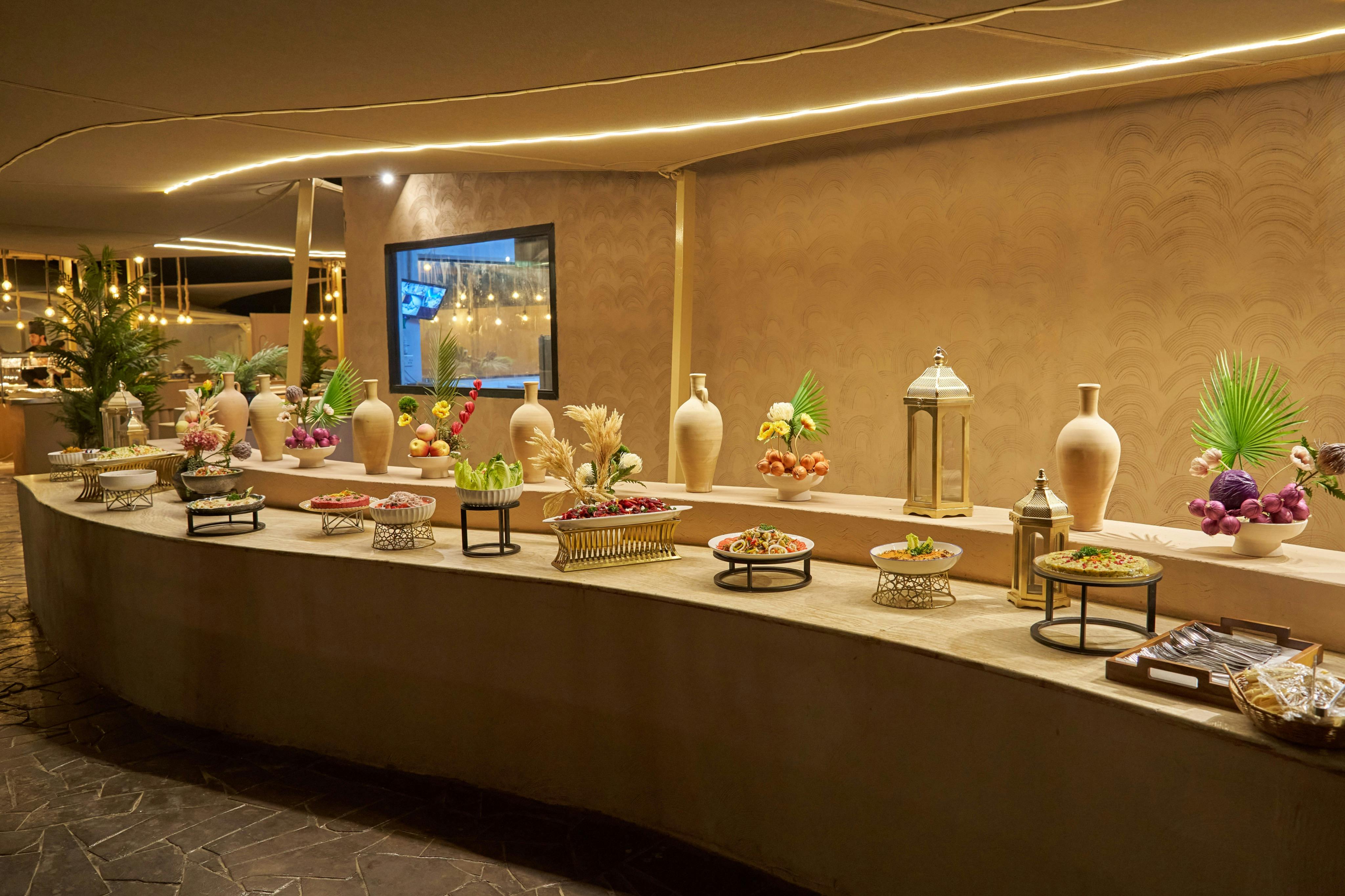 Elegantly arranged buffet table with decorative vases, plants, and various dishes on stands in a warmly lit room.
