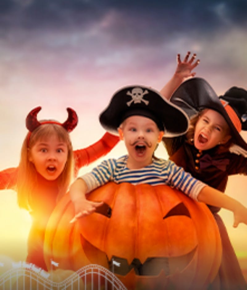 할로윈 의상을 입은 세 명의 어린이 (악마, 해적, 마녀) 가 석양에 커다란 조각 호박 뒤에서 신나게 포즈를 취하고 있습니다.