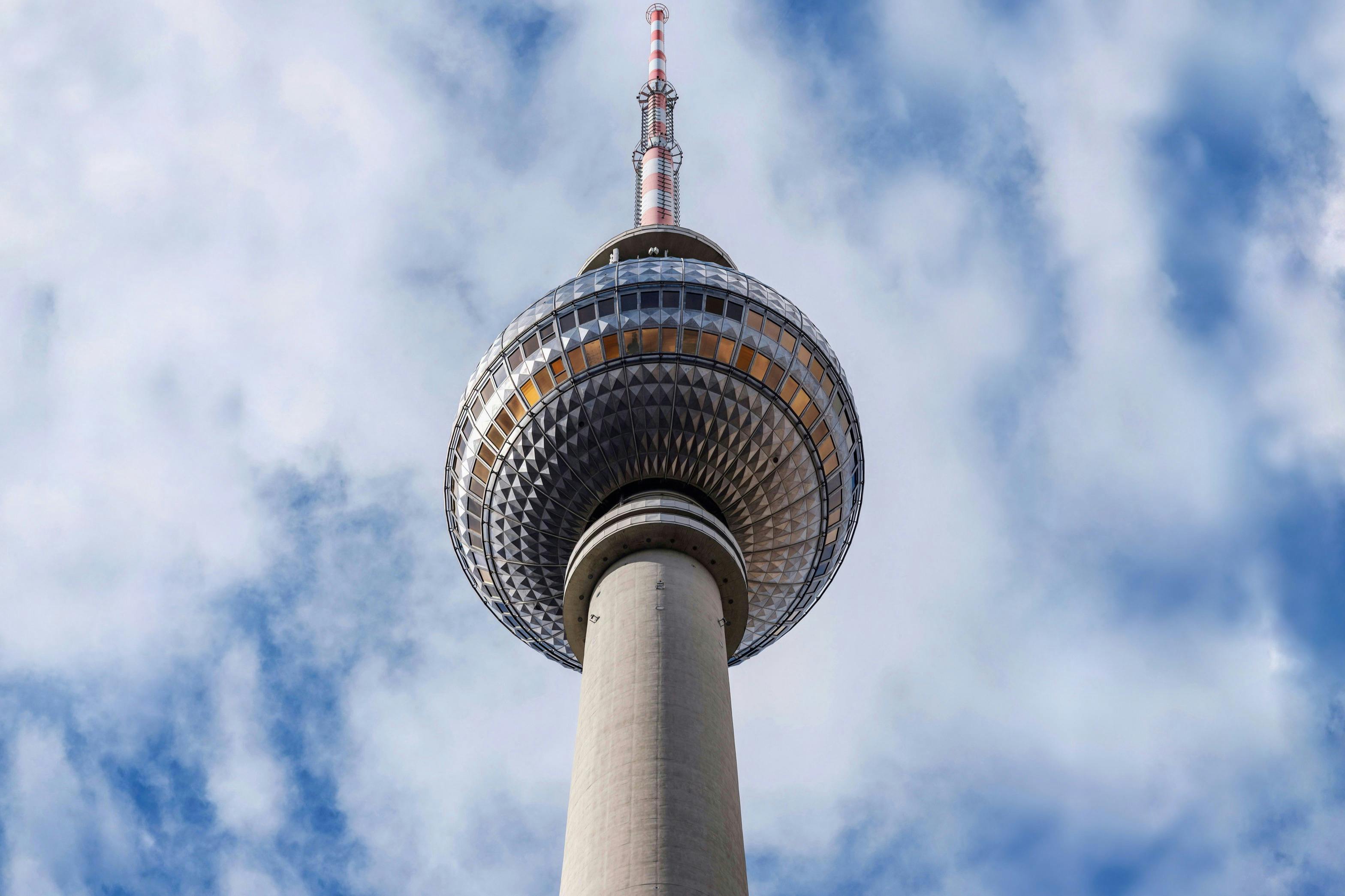 Ein hoher Fernmeldeturm mit einer kugelförmigen Aussichtsplattform vor einem bewölkten Himmel.