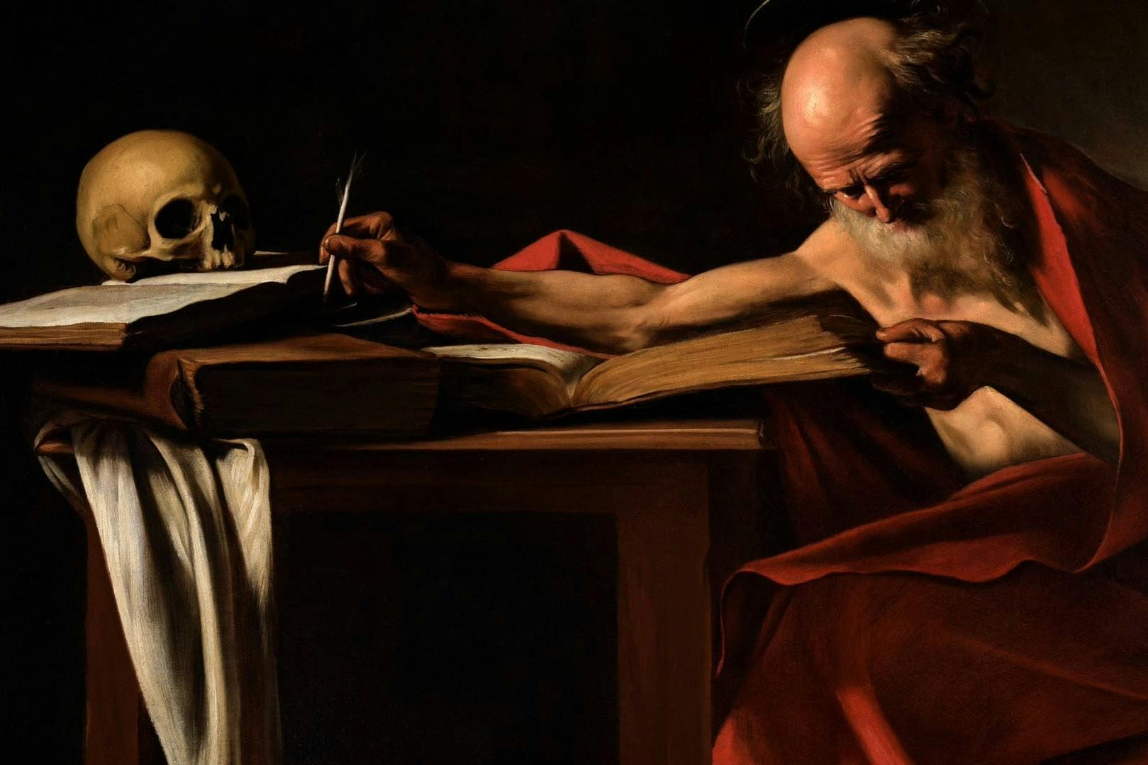 Una mano che tiene una penna d'oca è appoggiata su un libro accanto a un teschio, con un drappo visibile sul bordo del tavolo.