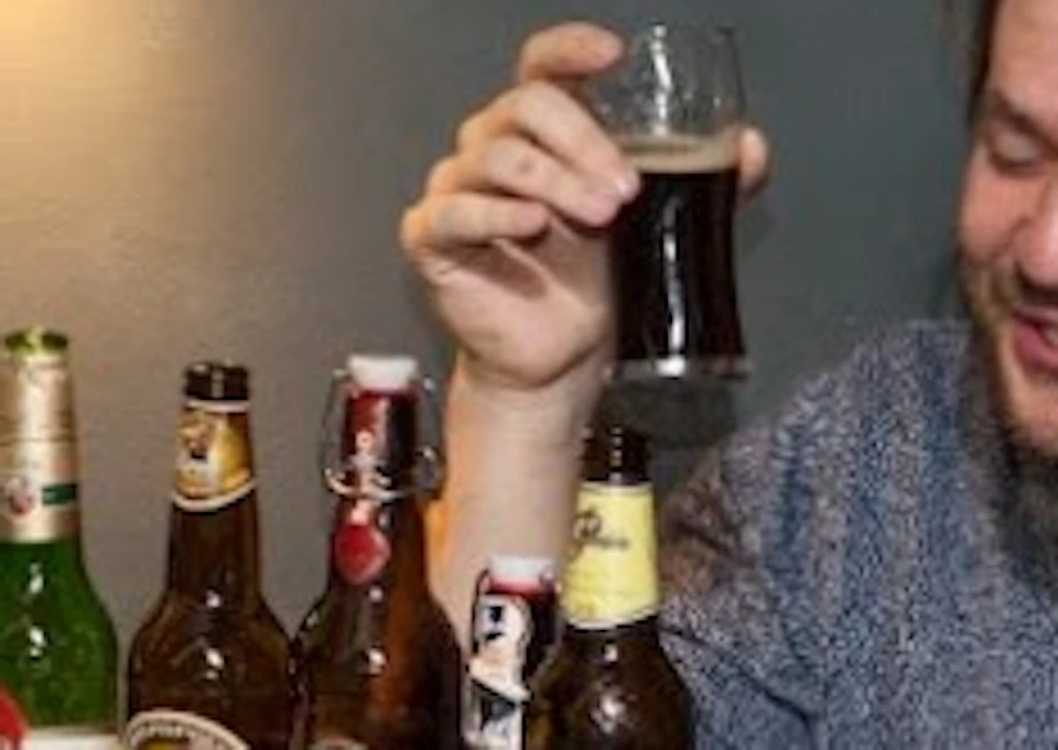 Group of friends laughing and holding beer glasses at a table with various beer bottles and glasses.