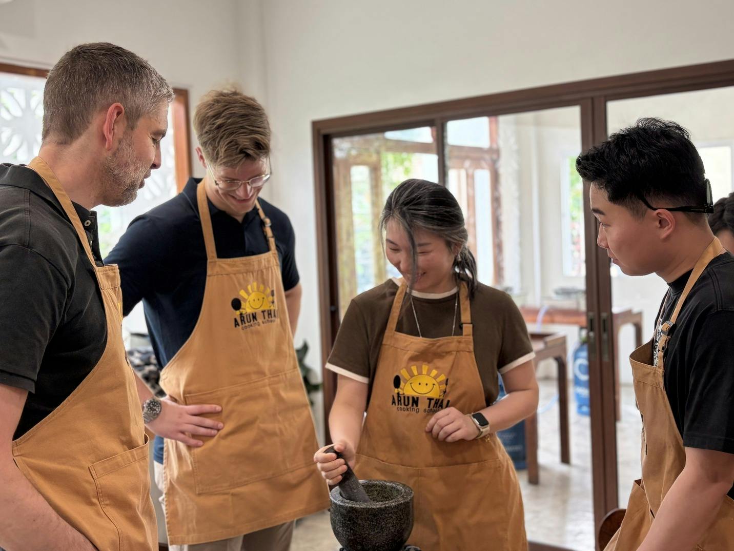 A group of people wearing aprons standing around a table, with one person using a mortar and pestle.