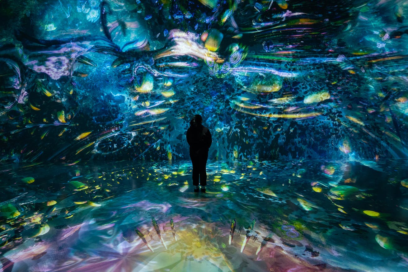 A person stands in a colorful, immersive digital art installation with vivid abstract patterns and light projections.