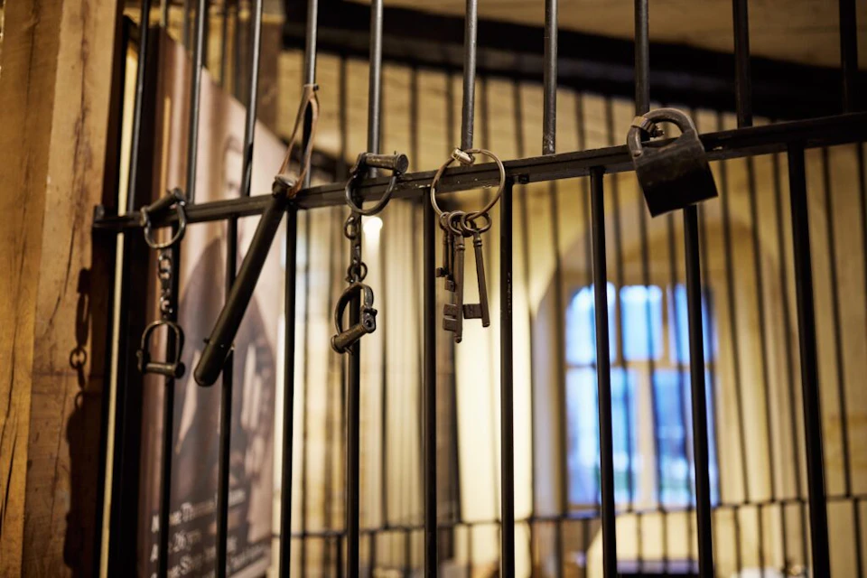 Several old-fashioned keys and locks hanging on metal bars, with blurred interior and arched window in the background.