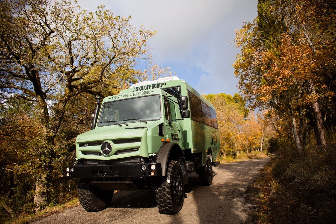 Ένα πράσινο όχημα εκτός δρόμου Mercedes 4x4 είναι σταθμευμένο σε έναν στενό δρόμο που περιβάλλεται από φθινοπωρινά δέντρα.