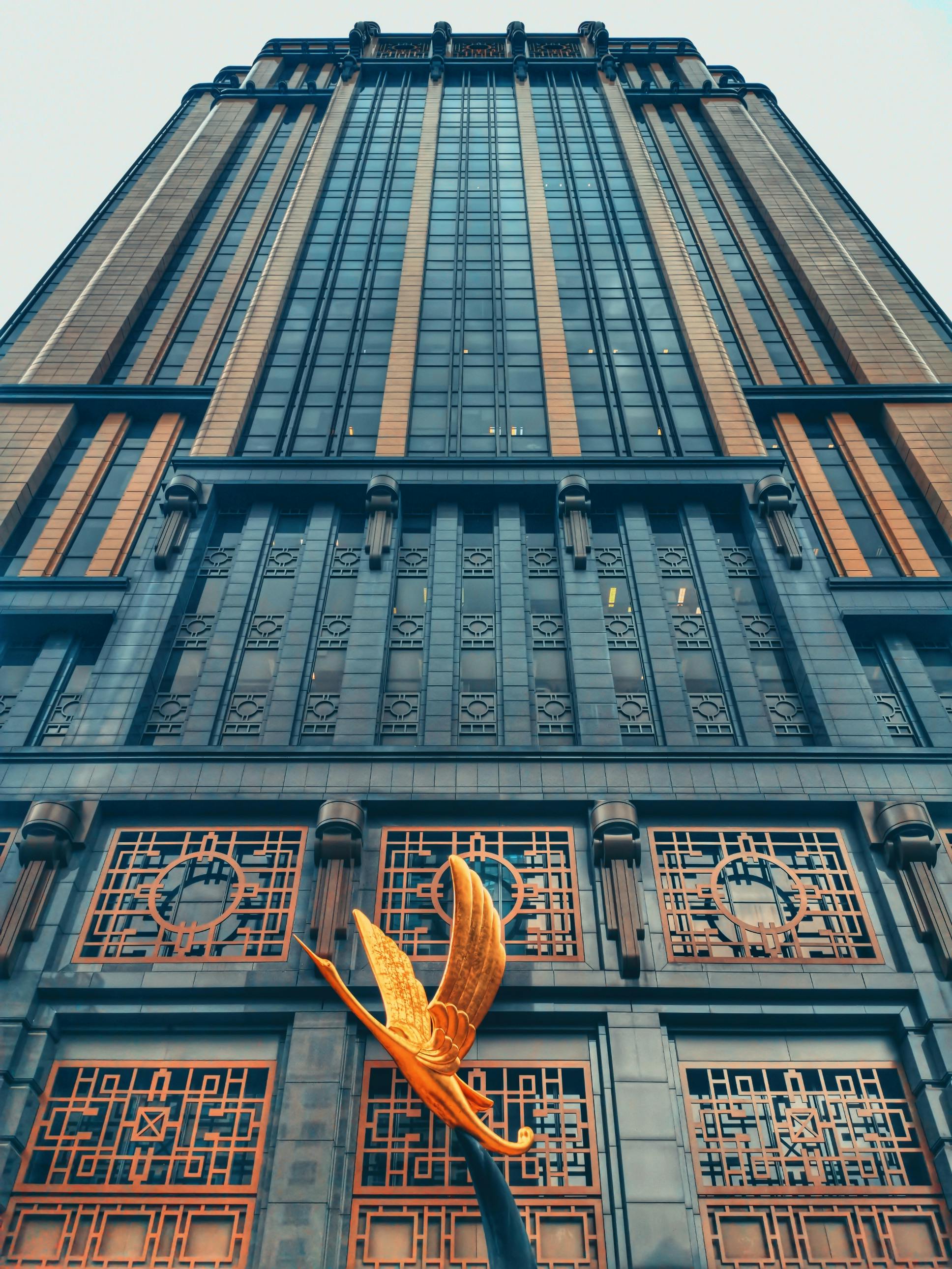 Tall building with ornate windows and geometric patterns, featuring a golden butterfly sculpture at the entrance.