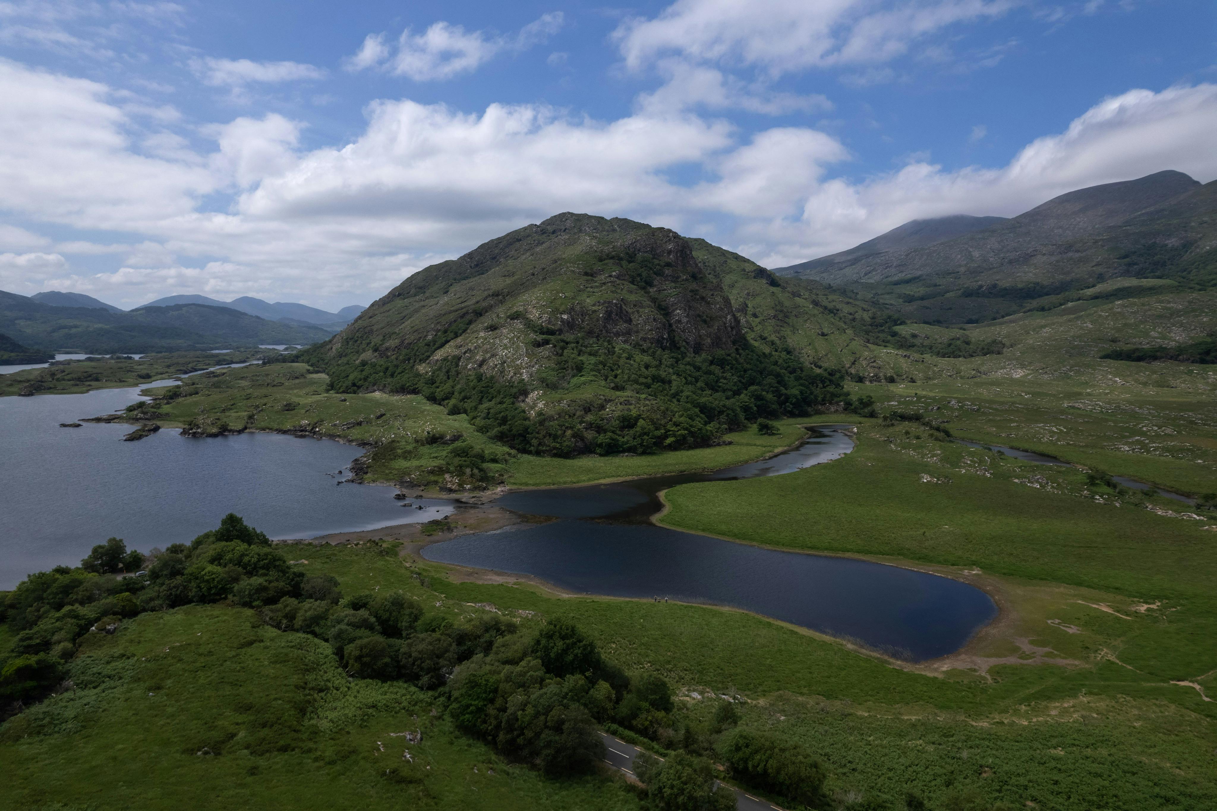 A scenic view of a grassy landscape with hills, a lake, and a partly cloudy blue sky.