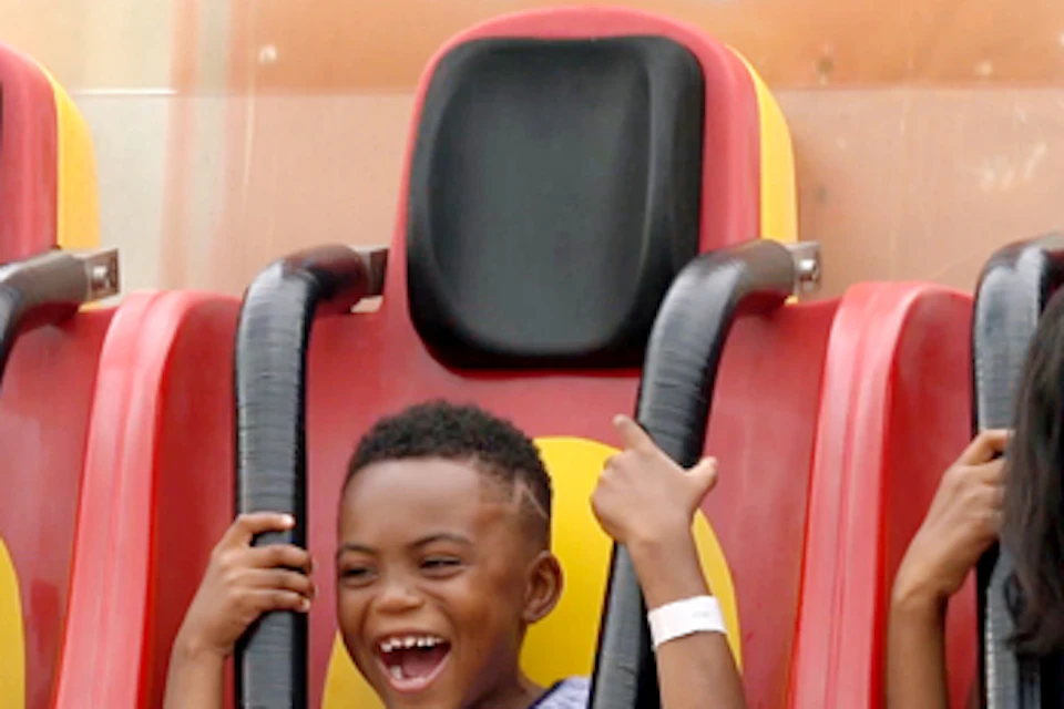 Three people, including a child, are seated on an amusement ride, laughing and holding on to their harnesses.