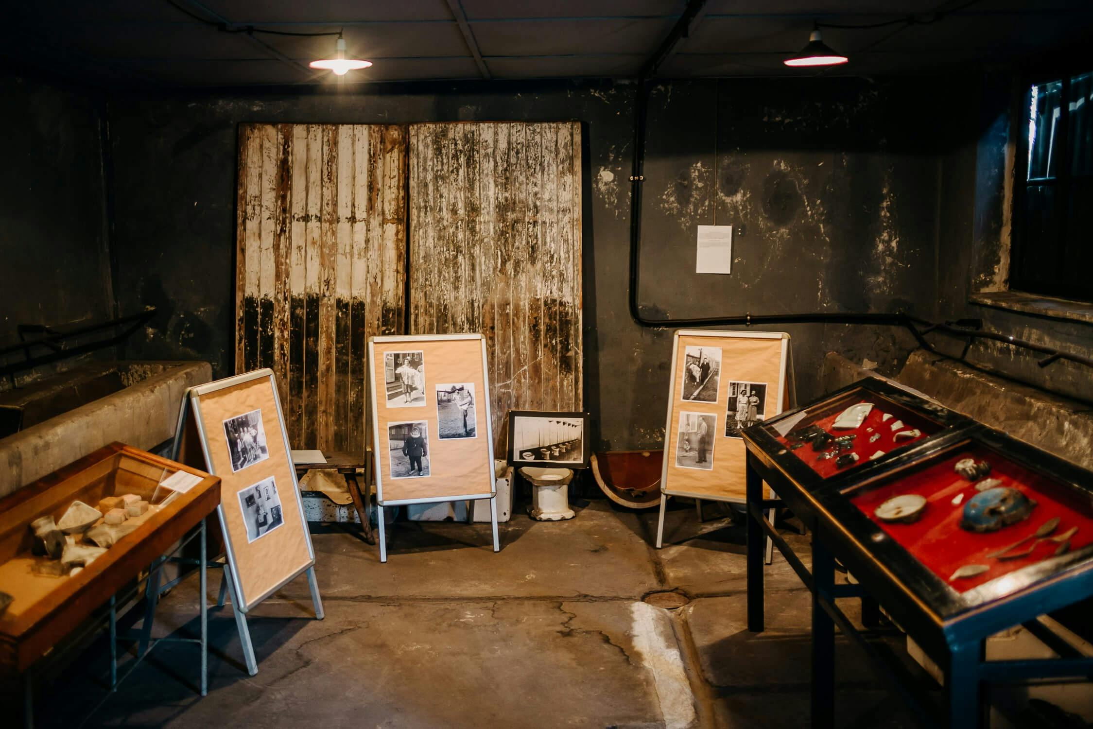 Et svagt oplyst rum med fotodisplays på staffelier, et indrammet billede på gulvet og glasdisplays.