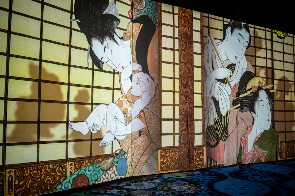A projection of traditional Japanese art depicting figures in colorful attire, shown indoors with patterns on the floor.