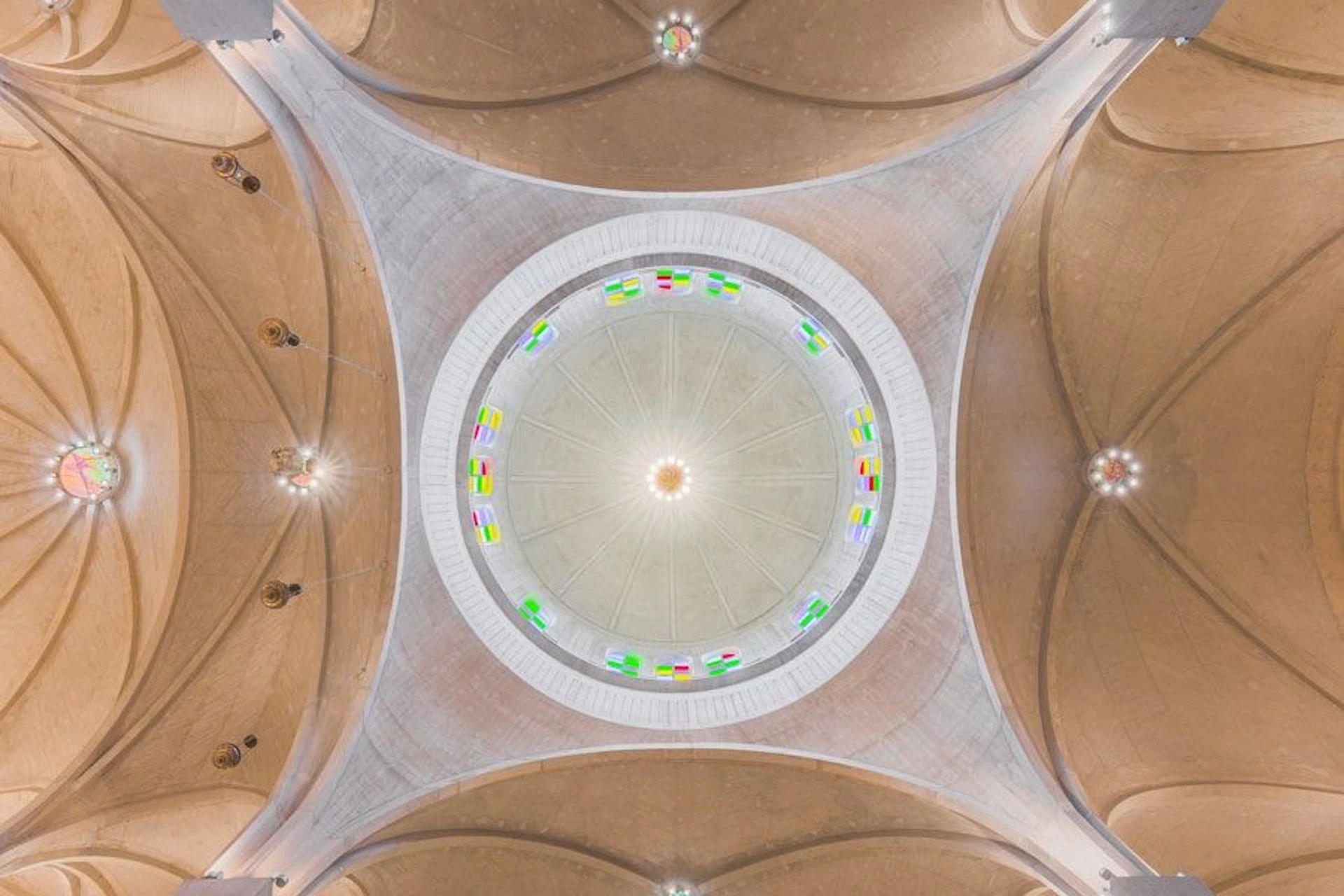 A symmetrical view of a dome ceiling with colorful stained glass windows encircling its base, set against a beige structure.