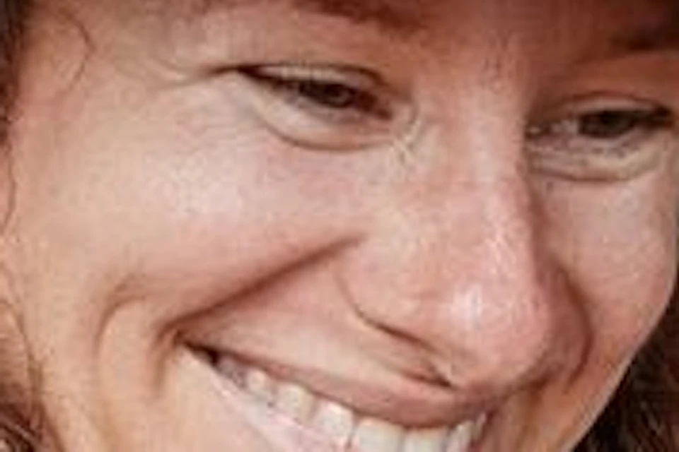 A smiling person wearing a hat holds an opened cacao pod on a table surrounded by tropical flowers and greenery.