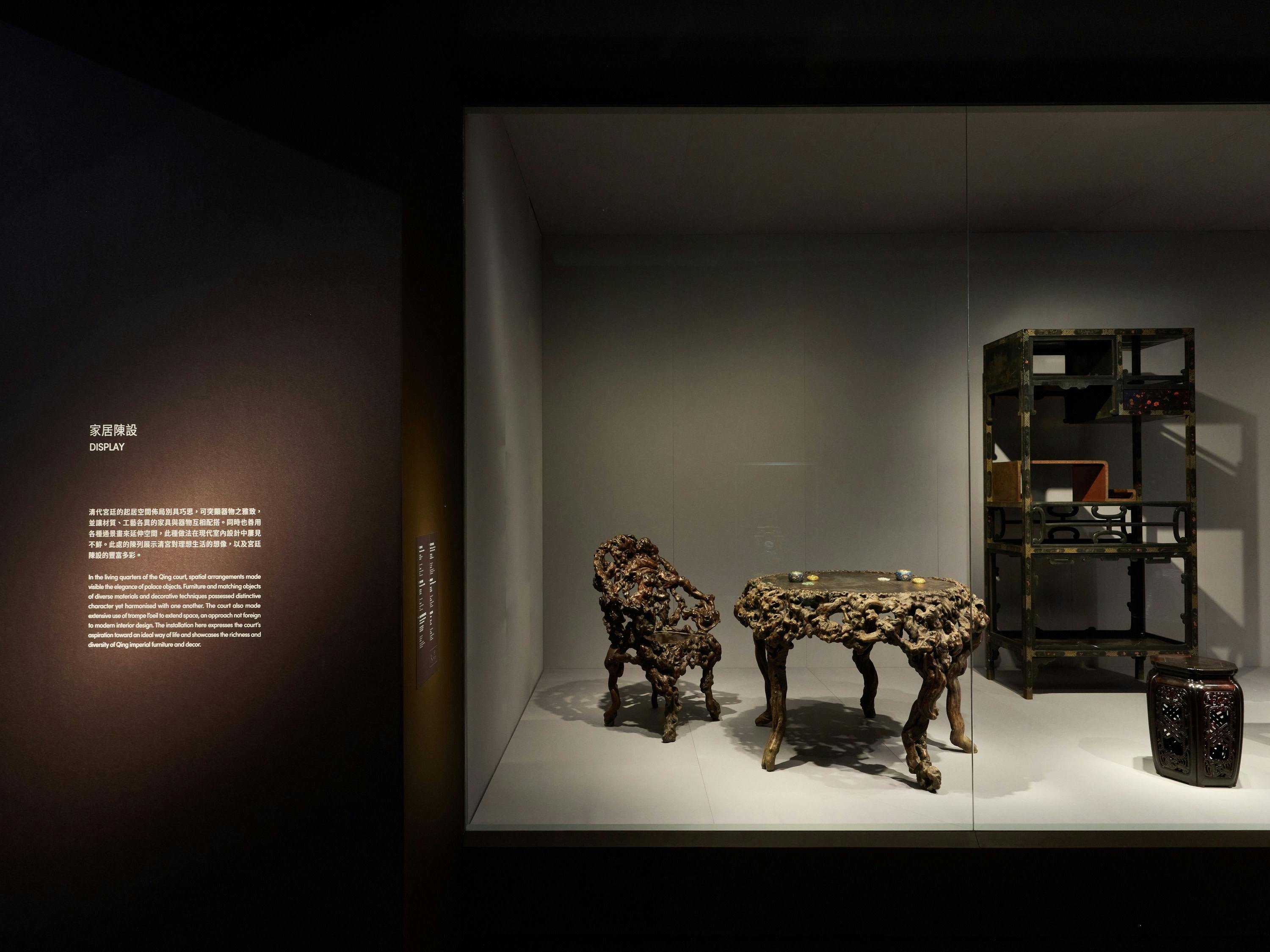An exhibit featuring ornately carved wooden furniture, including a chair and a table, displayed in a glass case.