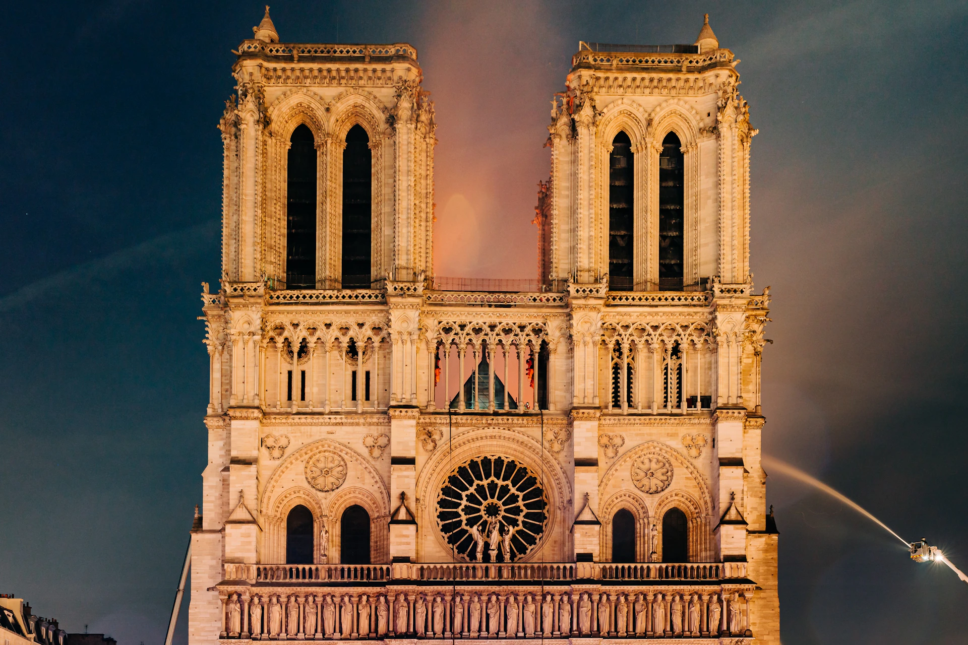Front view of Notre-Dame Cathedral with its iconic twin towers and central rose window illuminated against a dark sky.