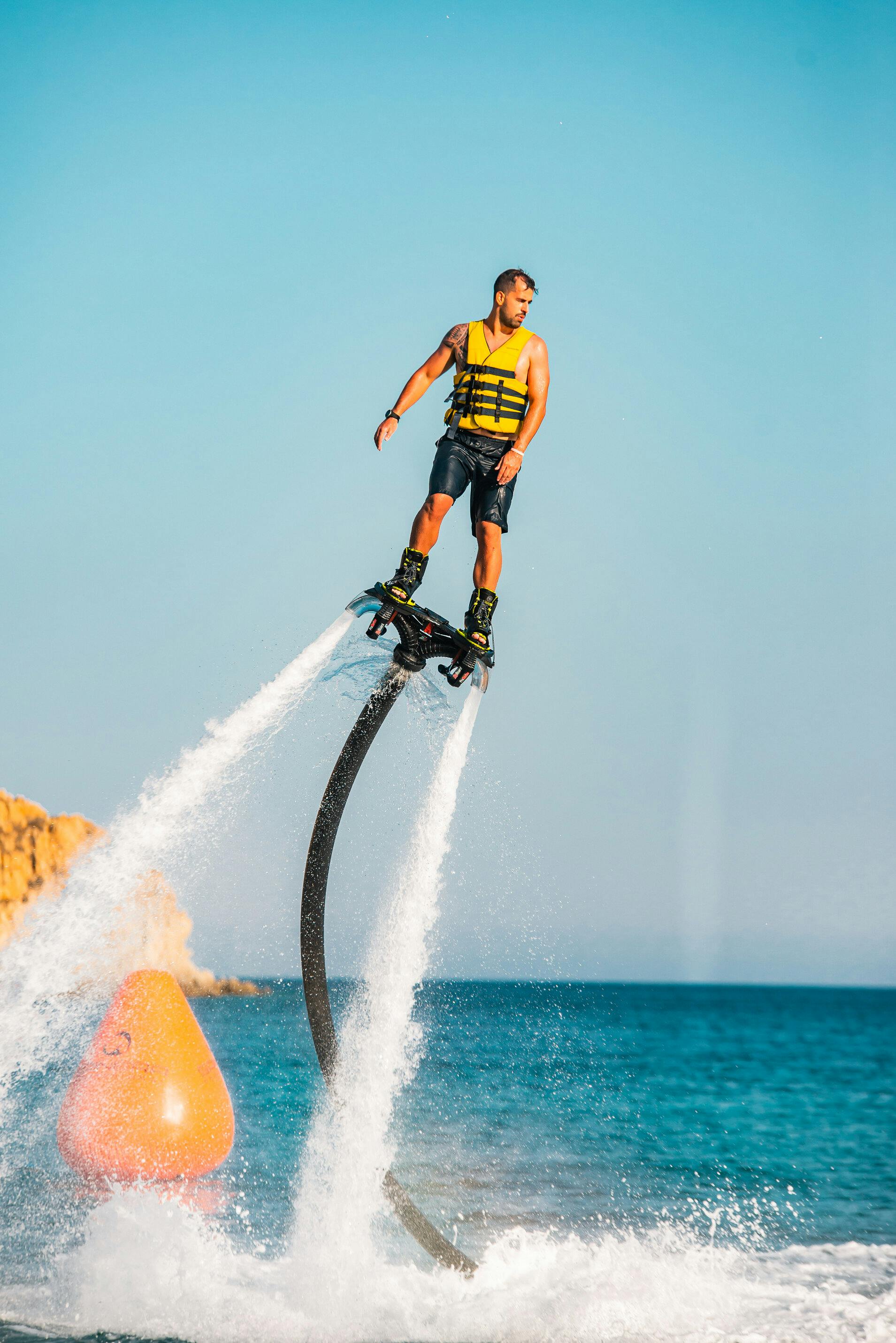 노란색 구명조끼와 검은색 반바지를 입은 사람이 맑고 푸른 하늘을 배경으로 물 위로 호버보드를 타고 있습니다.