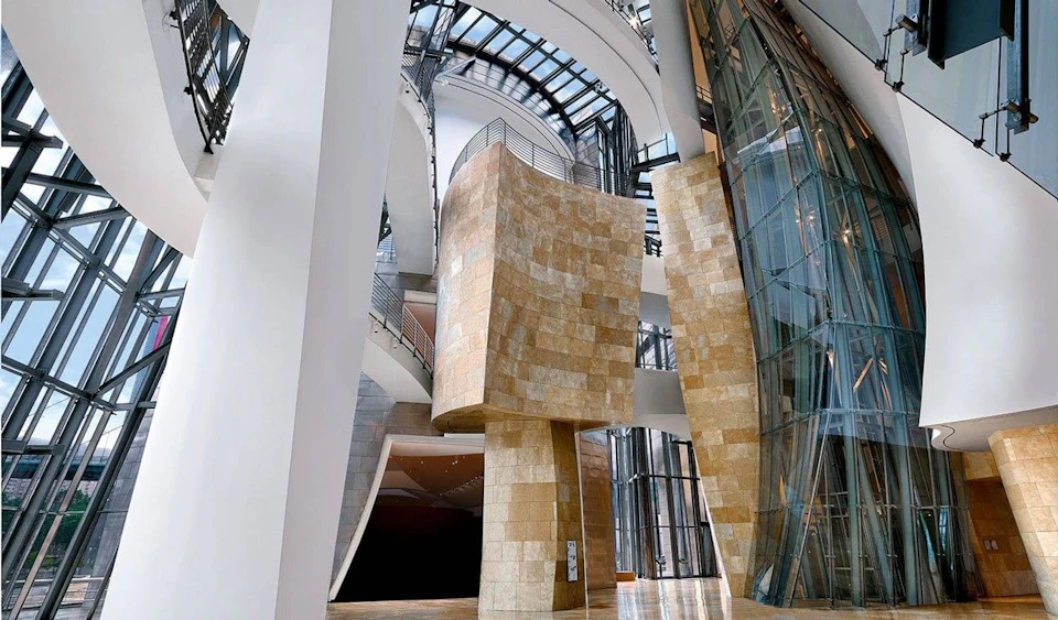 Modern interior with curved stone and glass structures, high ceilings, and a mezzanine with metal railings.