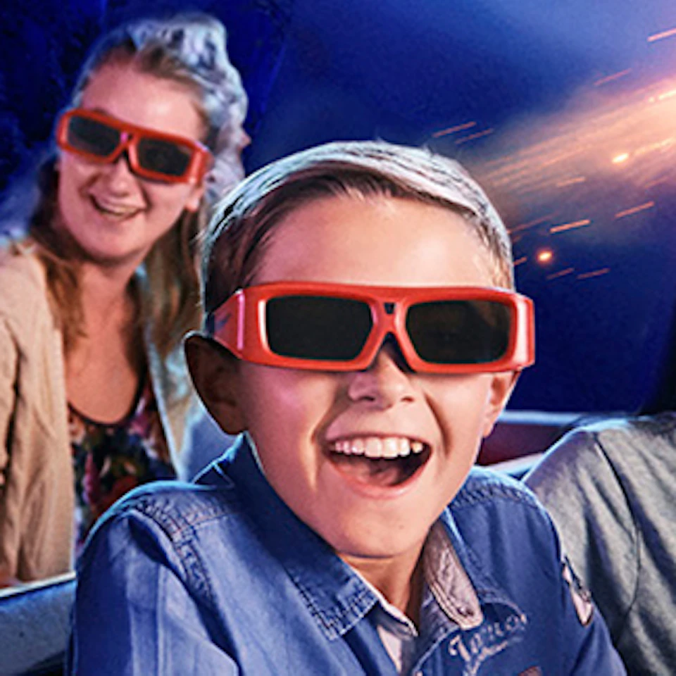 People wearing 3D glasses excitedly watch an animated panda flying past them in a themed attraction ride.